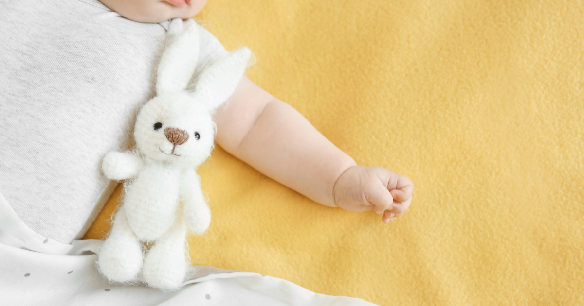 ぬいぐるみを抱いた赤ちゃんの腕とあたたかい毛布。子どもとの思い出を感じさせるやさしい一枚。