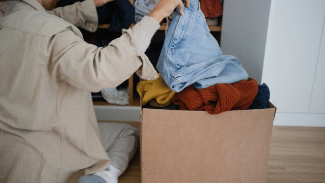 段ボールに服を入れながら仕分けする女性。手放す作業の途中を切り取ったシーン。