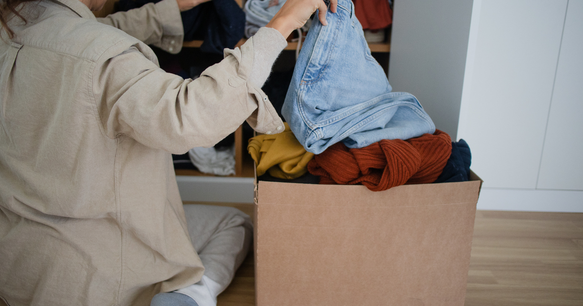 段ボールに服を入れながら仕分けする女性。手放す作業の途中を切り取ったシーン。